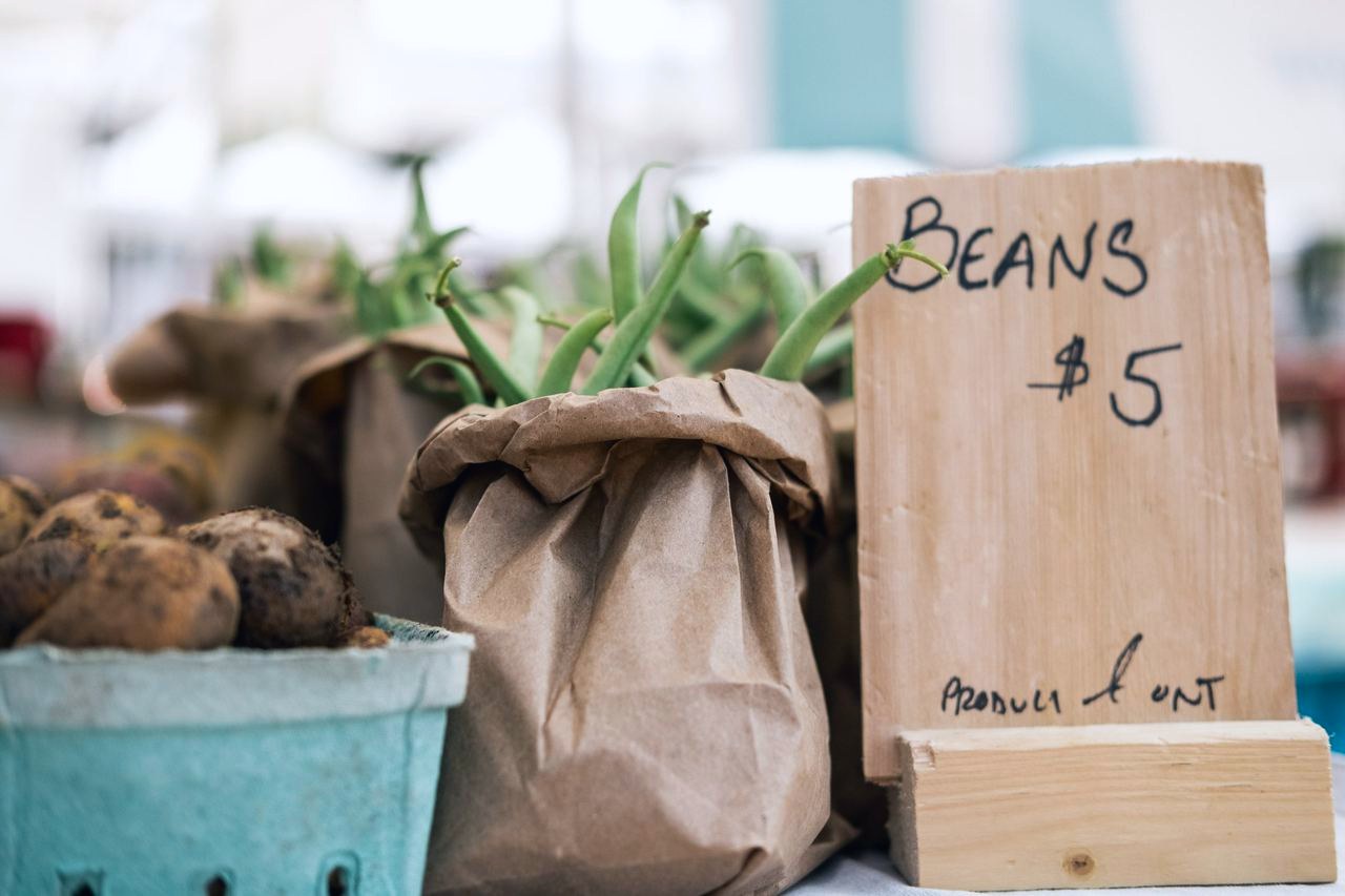 A farmers market table with a paper bag of beans and a hand-lettered price sign
