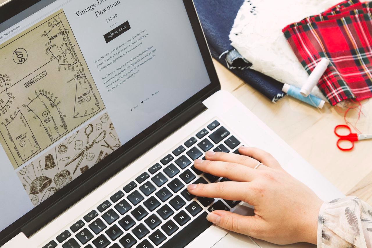 A hand typing on a laptop showing a small brand's online product page